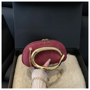 Macro view of burgundy suede round clutch bag featuring chunky gold metal handle and chain