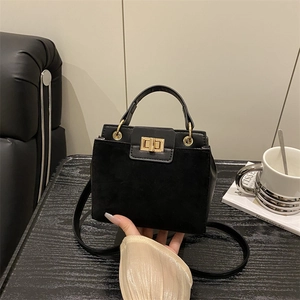 Minimalist black handbag with gold twist lock on dark wood desk with art book