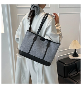Detail of grey felt tote bag with black leather straps worn over a white trench coat