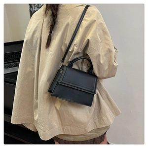Rear view of a black crossbody square bag with a knotted top handle on a person