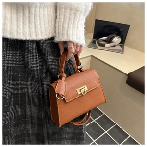 Detailed shot of caramel brown lychee leather handbag with golden metal twist lock closure
