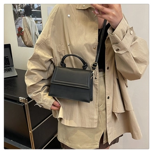 Detail of black crossbody square bag with unique twisted handle and adjustable strap