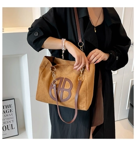 Brown faux suede tote bag with leather handles and gold chain details shown on a model
