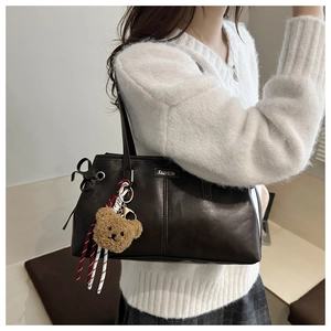 Detailed close-up of brown tote bag with metal Fashion plate and cute plush bear charm