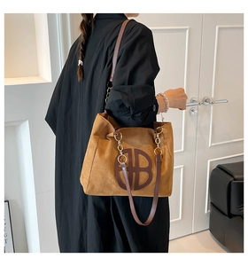 Macro shot of large tan suede tote bag featuring hollow circular logo and metal chain strap