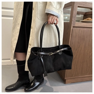 Detail of black suede tote bag with metal clasp shown on model in a long beige coat