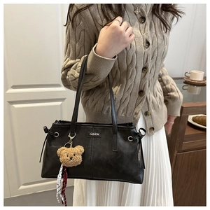 Detail of black leather tote bag featuring a plush bear charm and fashion label