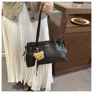 Detail of black faux leather tote bag featuring fashion label and plush bear charm decoration