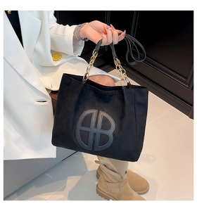 Detail of black suede tote bag featuring a gold chain strap and hollow AB logo design
