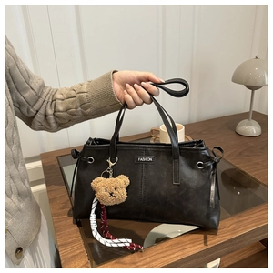 Detail of black tote bag featuring a teddy bear charm and fashion label embellishment