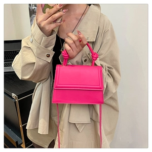 Detail of a bright magenta crossbody bag with knot handle and adjustable shoulder strap