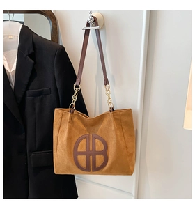 Close-up of brown suede tote bag featuring a circular logo and leather gold chain strap