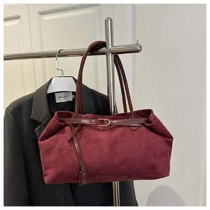 Detail of burgundy suede tote bag featuring a gold D-ring buckle and brown leather straps