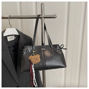 Detail of black faux leather shoulder bag with fashion plaque and plush bear charm