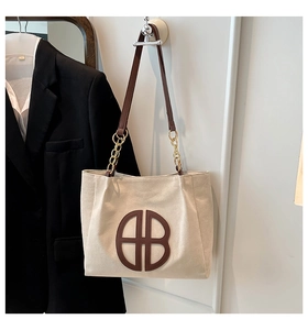 Detail of the large beige canvas tote bag with brown HB leather patch and chain strap