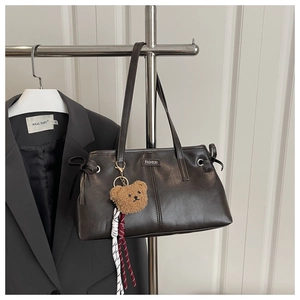 Detail of dark brown matte leather tote bag featuring a FASHION metal plate and bear charm