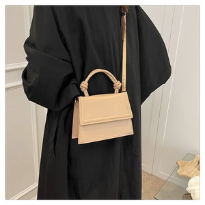 Close-up of minimalist cream crossbody bag with knotted handle detail and adjustable strap