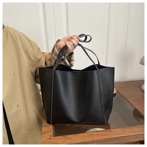 Detail view of a large black matte leather tote bag with slim handles in a lifestyle setting