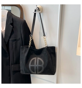 Detail of black suede tote bag with decorative AB stitching and gold chain strap