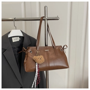 Detail of vintage brown tote bag with fashion logo, teddy bear charm and side drawstring