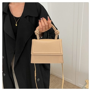 Detail of beige trapezoid handbag with knotted handle design on a black coat outfit