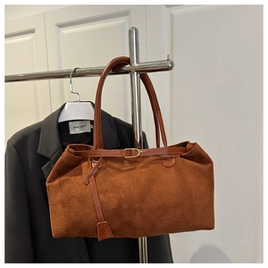 Detail of a brown suede tote bag featuring a leather strap and gold metal buckle finish