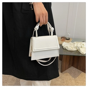 Detail of white leather handbag featuring unique knotted handles and a sleek flap closure