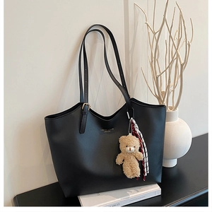 Detail of black faux leather tote bag featuring gold hardware and a cute bear charm