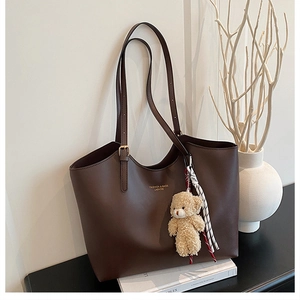 Detail of vintage dark brown tote bag with plush bear charm and minimalist logo