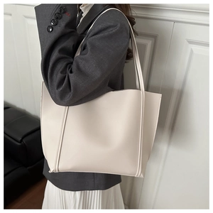 Detailed close-up of a large beige tote bag worn with a professional blazer and skirt