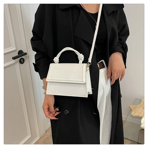 Close-up of white structured handbag with decorative knot handle and leather strap