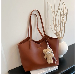 Close-up of brown leather tote bag with FASHION & BAGS logo and plush bear charm