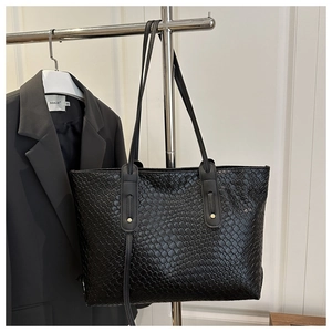 Detail of black woven tote bag showing dense cross-texture and golden metallic accents