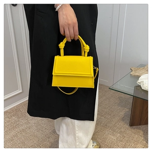 Close-up of bright yellow mini handbag featuring a twisted handle and adjustable strap