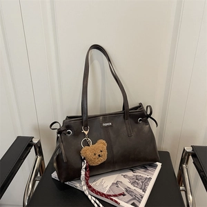 Dark brown leather tote bag with silver eyelets and plush bear charm on a black chair