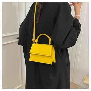 Detail of bright yellow minimalist crossbody bag on a black coat with knot handle