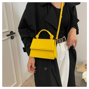 Model wearing a bright yellow faux leather crossbody square bag with a black coat