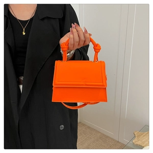 Detail of bright orange square crossbody bag featuring unique double knot handle design
