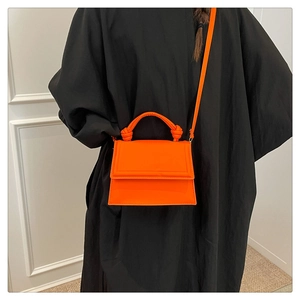 Detailed view of bright orange mini bag with knotted handle and magnetic flap closure