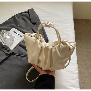 Detail of a creamy pleated cloud bag with slim handles and metallic buckle on white linen