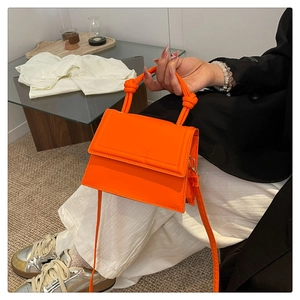 Fluorescent orange structured handbag shown with casual blazer and striped pants