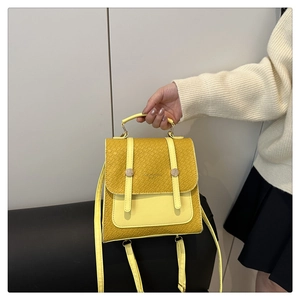 Close-up of yellow handbag featuring woven texture flap and decorative metal straps