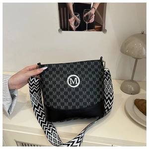 Detail of the letter M pattern leather bag with a wide geometric woven shoulder strap
