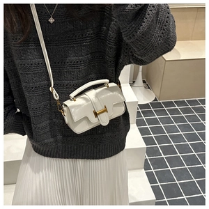Detail of white patent leather mini bag featuring gold H-shaped clasp and top handle