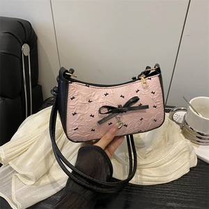 Pink pleated underarm bag with black bow and heart pendant shown being held by hand