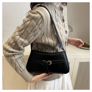 Detail of minimalist black leather underarm bag with metal buckle strap on a beige sweater
