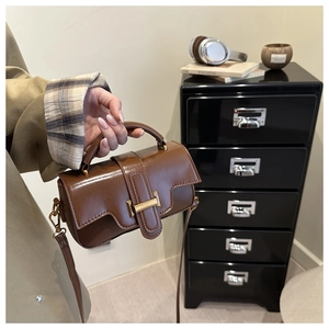 Detail of dark brown leather handbag with metallic buckle held by a woman in a trench coat