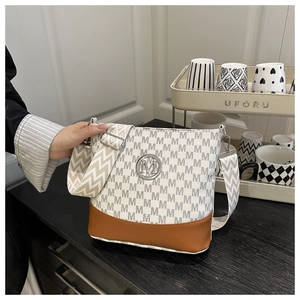 Detail of monogram bucket bag featuring metal M logo and wide woven shoulder strap