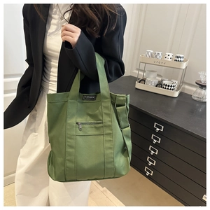 Detail of green canvas tote bag featuring a functional zipper pocket and fashion patch