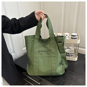 Green canvas tote bag detail showing functional front zipper pocket and adjustable strap